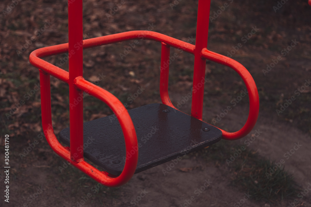 Empty children's swing red color close-up. The concept of sadness, loss, death, mourning, orphanhood or loneliness. Empty children's swing red color close-up. The concept of sadness, loss, death, mourning, orphanhood or loneliness.