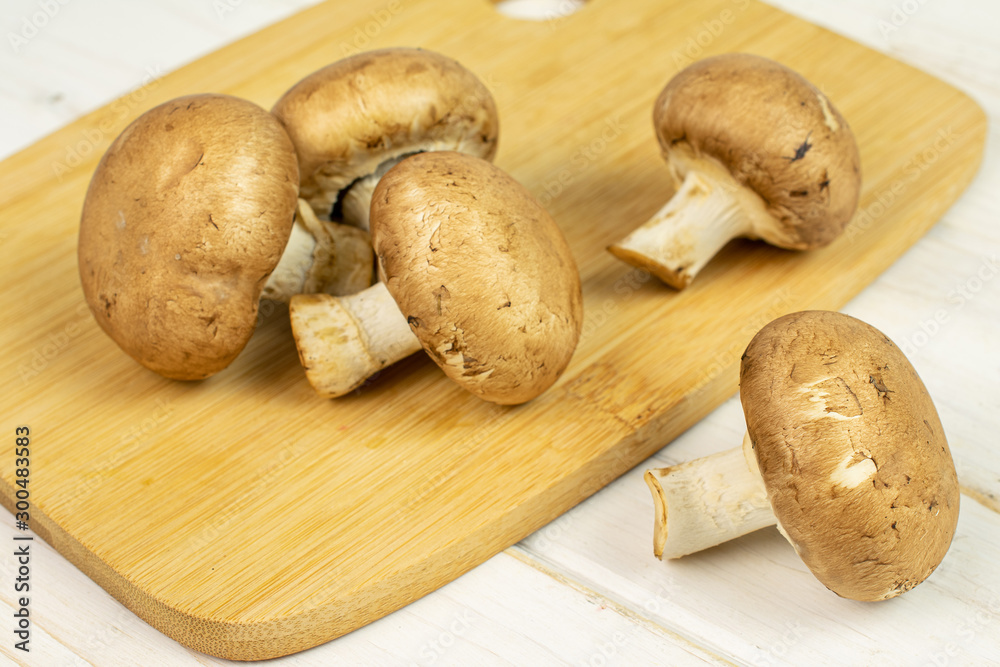 Group of five whole fresh brown champignon on bamboo cutting board on white wood Group of five whole fresh brown champignon on bamboo cutting board on white wood