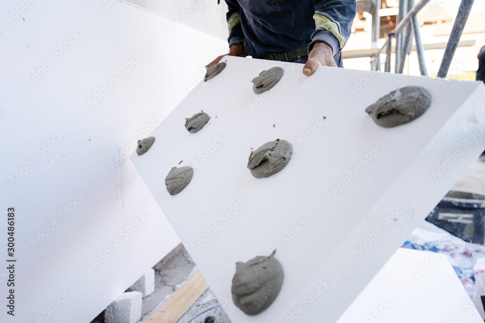Worker placing styrofoam sheet insulation to the wall at construction ...