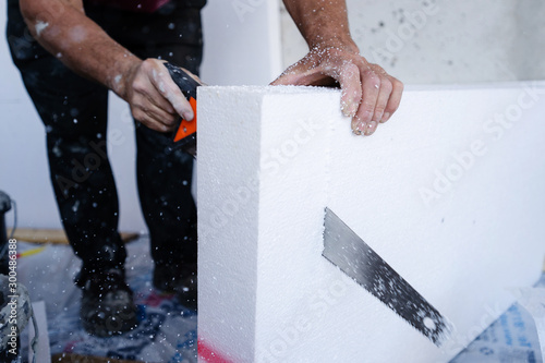 Construction worker using the hand saw to cut the styrofoam insulation panel table at the construction site in the insulating renovation procedure