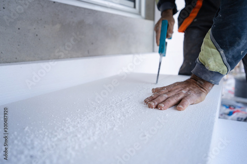 Construction worker using the hand saw to cut the styrofoam insulation panel table at the construction site in the insulating renovation procedure photo