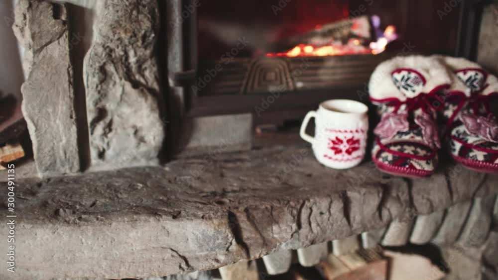 Christmas Comfortable Slippers by the Warm Cozy Fireplace. 4K STABILIZED. Relaxing atmosphere in a chalet by authentic vintage fireside with a cup of hot drink. Winter and Christmas holidays concept. 