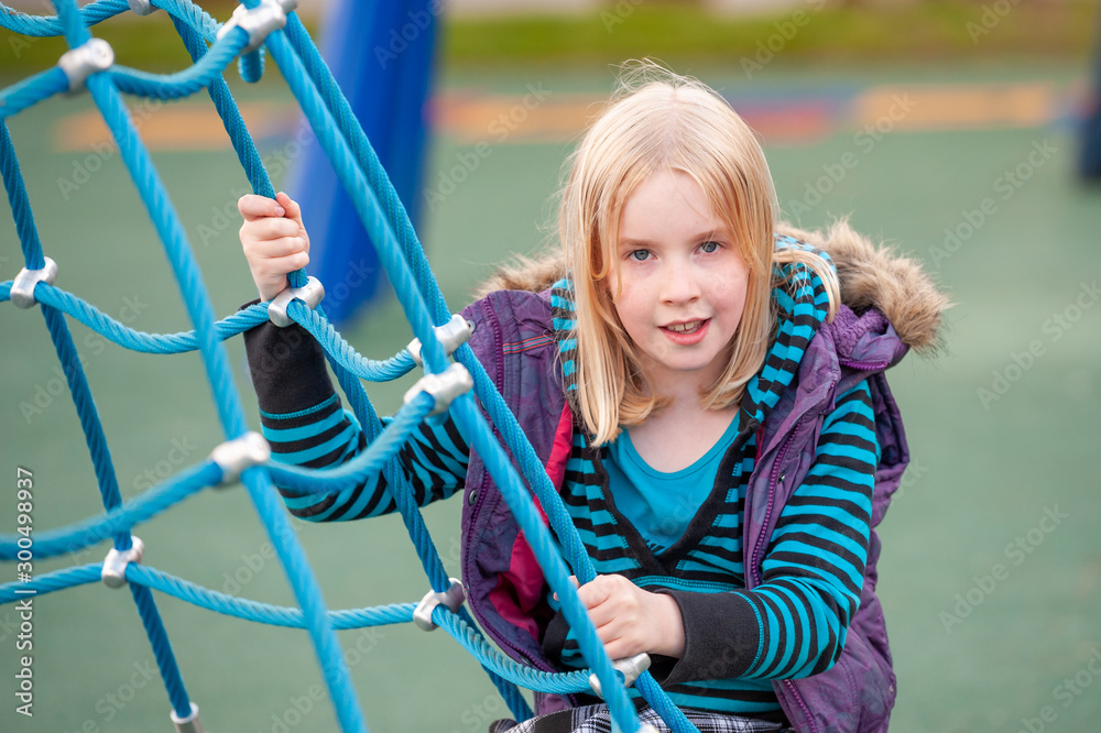 Pretty young blonde girl climbing on a rope ladder in a playground Stock  Photo