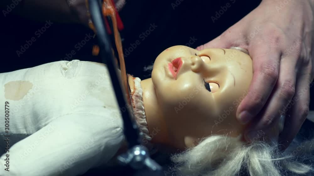 male hands saw off a scary dolls head, halloween