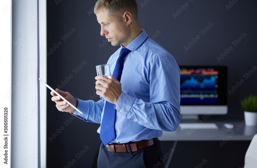 Smiling businessman with touchpad standing at workplace in office Smiling businessman with touchpad standing at workplace in office