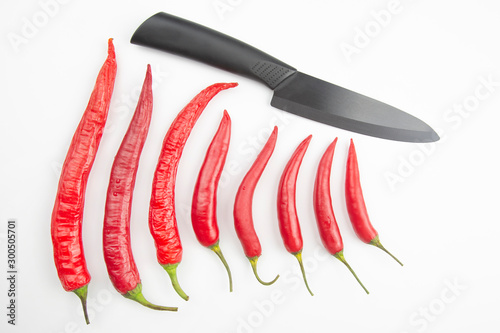 Red hot pepper and black ceramic kitchen knife on white background. Healthy vegetable food and vitamins.