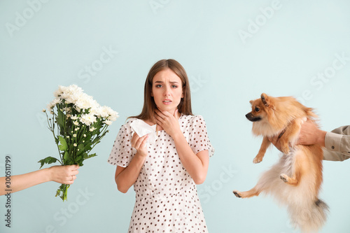 People giving flowers and dog to young woman suffering from allergy on light background photo