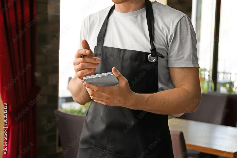 Obraz premium Young male waiter with notebook in restaurant, closeup