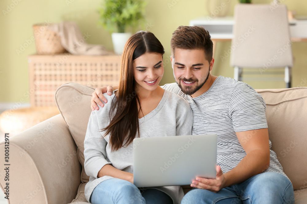 Portrait of beautiful young couple with laptop at home