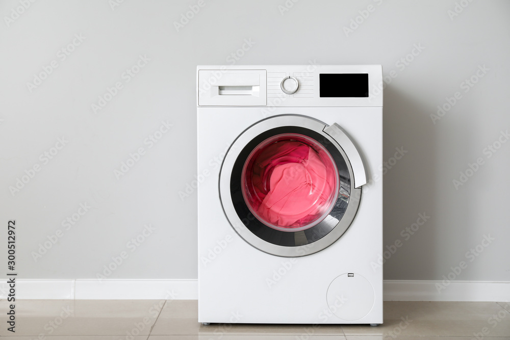 Modern washing machine with laundry near white wall