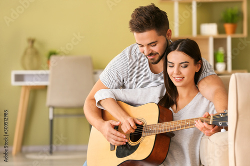 Beautiful young couple playing guitar at home