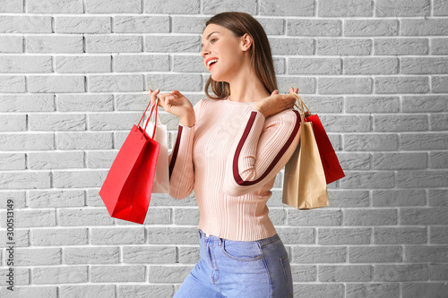 Beautiful young woman with shopping bags on brick background