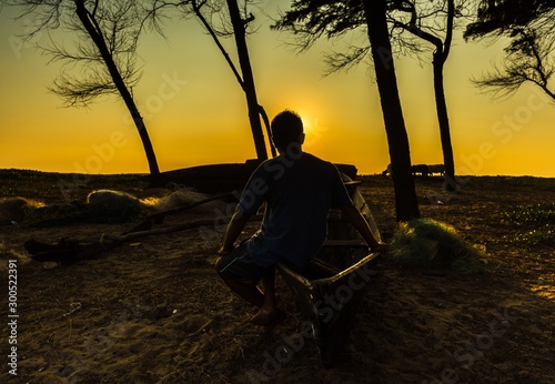 silhouette of a man sitting on a boat looking at evening sun, Pollem, Goa, India photo