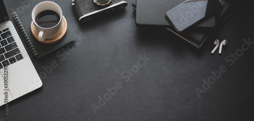 Top view of dark trendy workspace with laptop computer, coffee cup and office supplies