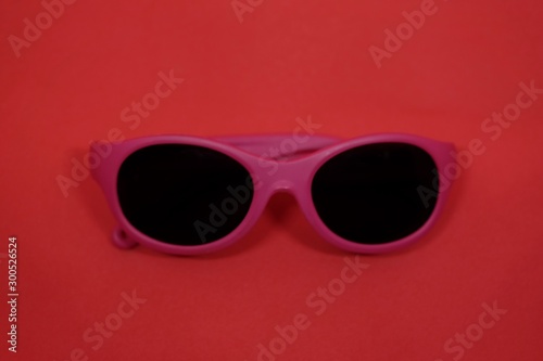 Pink plastic sunglasses isolated on red background.