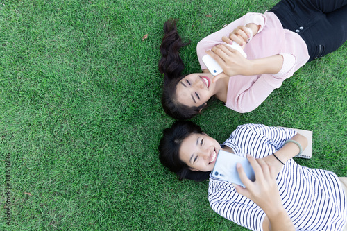 Happy young Asian woman two people using phone surf internet while laying down on grass together. lifestyle, Communication and technology concept. with Copy space