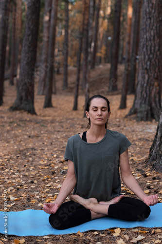 Relaxed woman doing meditation while sitting in a forest with closed eyes among pine trees