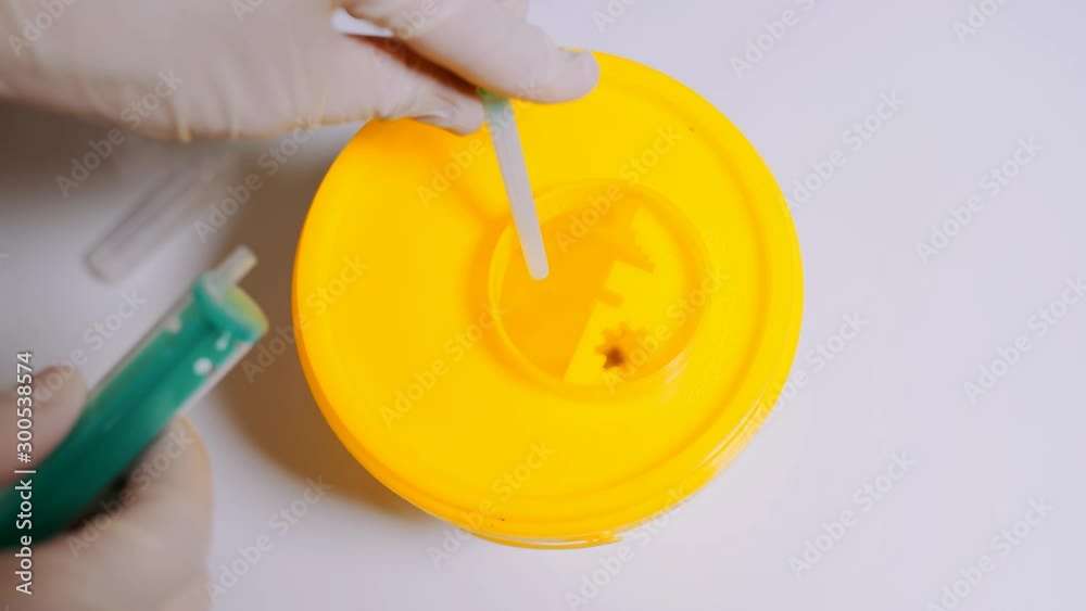 Container for disposing of used syringes. A healthcare professional throws a used syringe into a container. Container for disposing of used syringes. A healthcare professional throws a used syringe into a container.