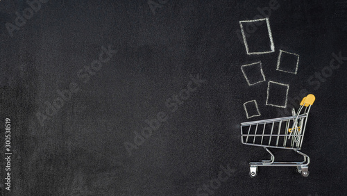 Shopping cart and products on chalkboard. Shop trolley at supermarket as sale, discount, shopaholism concept with copy space left for text or design. Top view or flat lay.