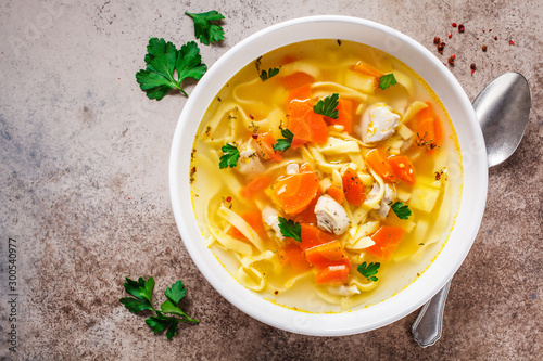 Chicken noodle soup with parsley and vegetables in a white plate, top view.