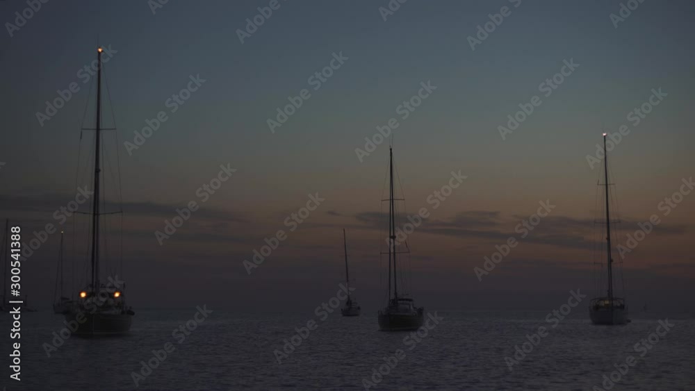 Many yachts in a bay on Formentera island. Incredible sunset in Cala Saona bay. Silhouettes of unrecognizable people on yachts Many yachts in a bay on Formentera island. Incredible sunset in Cala Saona bay. Silhouettes of unrecognizable people on yachts