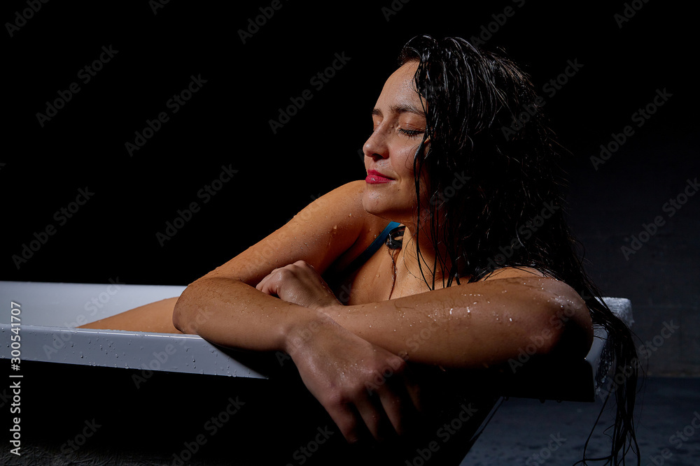 Young pretty brunette woman in bath with water and flowers in a dark room Young pretty brunette woman in bath with water and flowers in a dark room