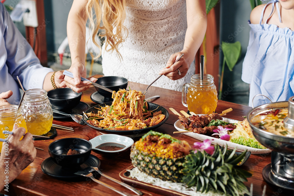Cropped image of housewife serving food at dinner table with various delicious dishes of Asian cuisine Cropped image of housewife serving food at dinner table with various delicious dishes of Asian cuisine