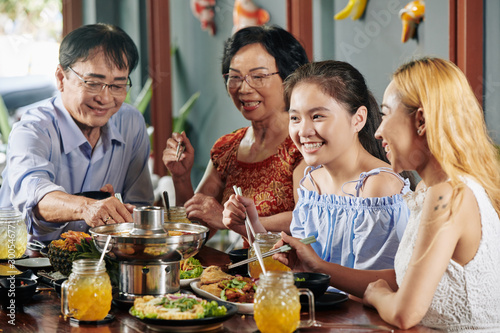 Happy preteen girl eating tasty dinner with her family in restaurant when celebrating some event together