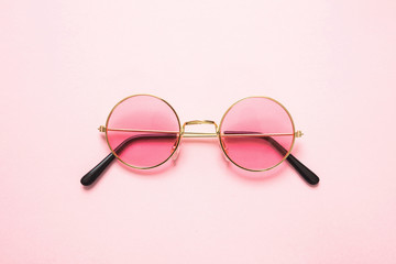 Golden frame sunglasses with pink lens on pink background, top view