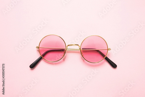 Golden frame sunglasses with pink lens on pink background, top view