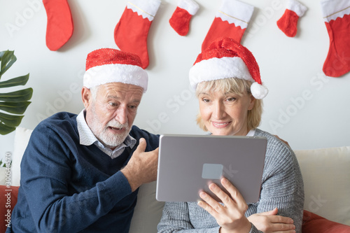senior elderly caucasian old man and woman, using conference on tablet with family together in living room that decorated for christmas festival day in the morning, retirement concept
