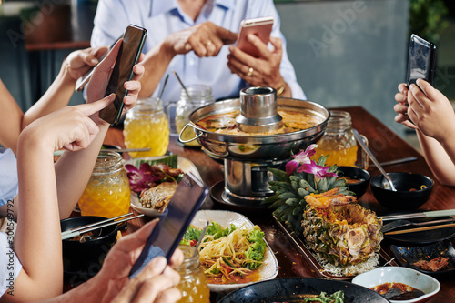 Hands of party guests sitting at dinner table with traditional Asian cuisine and texting friends of checking social media on smartphones