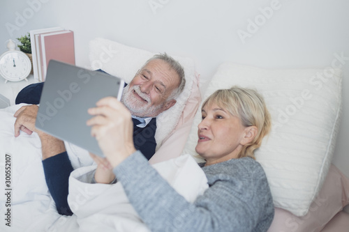 happy elderly couple caucasian senior man conferrencing with family by using on tablet in white blanket in bedroom, retirement love family lifestyle concept © FrameAngel