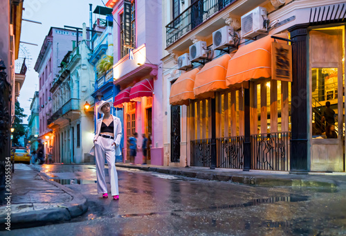 Photography Stylish woman in a white suit and white hat on a night street of Cuba