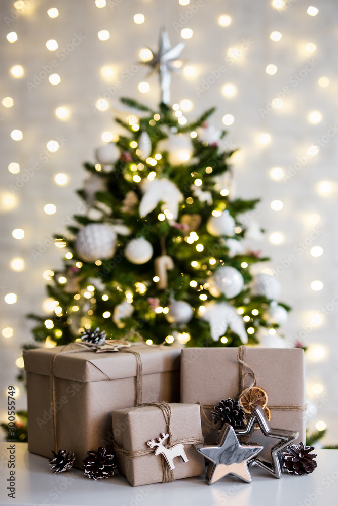 christmas and new year concept - beige gift boxes near decorated christmas tree over white wall with lights