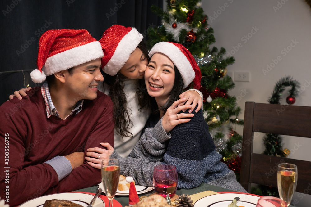 happy family, daughter smiling and kiss father mother and celebrate together at christmas day night in dining room that decorated with christmas tree for christmas festival day happy family, daughter smiling and kiss father mother and celebrate together at christmas day night in dining room that decorated with christmas tree for christmas festival day