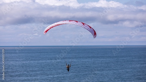 A man fly a paraglider over the dunes of Cape Kiwanda. Cloudy sky and the ocean waves in the background.