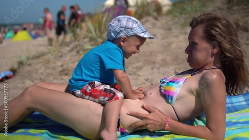 Pretty woman in swimsuit with her little boy at beach. Loving mom and her son