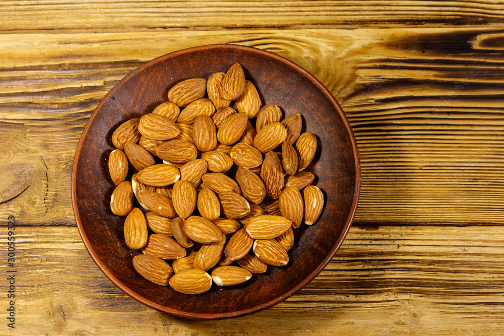 Almonds in ceramic plate on a rustic wooden table. Top view Almonds in ceramic plate on a rustic wooden table. Top view
