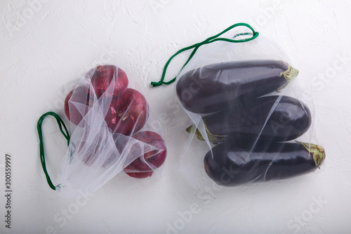 Eggplant and beets in textile grocery mesh bags. Purple fruits and vegetables in reusable eco friendly packaging on white background.