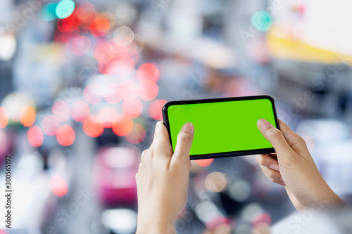 Woman hand using smart phone play game online, blank green screen on mobile, Bokeh traffic jam background.