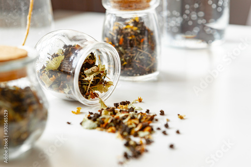 Glass jars with dry tea leaves close up on white table