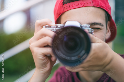 Teenage boy taking photos outdoors. Young man works reporter, outdoors. Caucasian guy holds a photo camera and capturing photos. 15 years old teenager is with digital photo camera