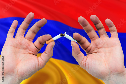 Armenia quit smoking cigarettes concept. Adult man hands breaking cigarette. National health theme and country flag background.