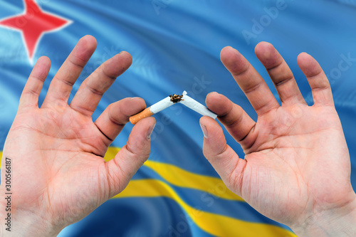 Aruba quit smoking cigarettes concept. Adult man hands breaking cigarette. National health theme and country flag background.