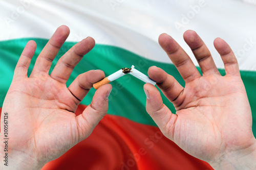 Bulgaria quit smoking cigarettes concept. Adult man hands breaking cigarette. National health theme and country flag background.