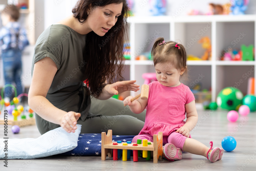 Cute woman and kid girl playing educational toys at kindergarten or daycare