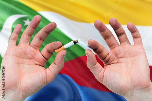 Comoros quit smoking cigarettes concept. Adult man hands breaking cigarette. National health theme and country flag background.