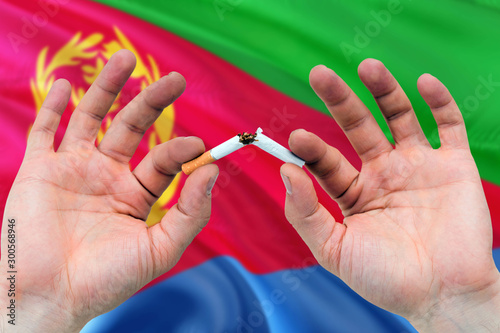 Eritrea quit smoking cigarettes concept. Adult man hands breaking cigarette. National health theme and country flag background.