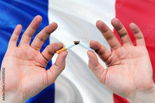 France quit smoking cigarettes concept. Adult man hands breaking cigarette. National health theme and country flag background.